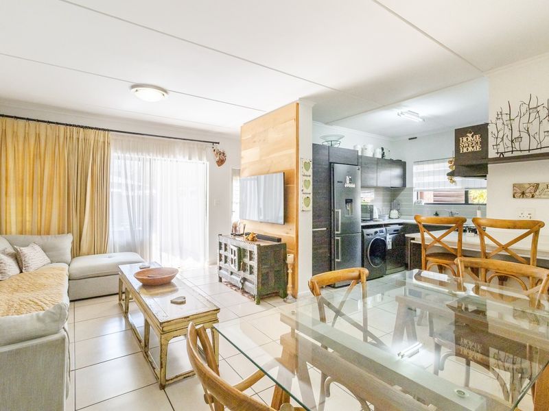 An open-plan living, dining, and kitchen area featuring tiled floors, a wood-paneled feature wall, and direct access to a patio through sliding glass doors.