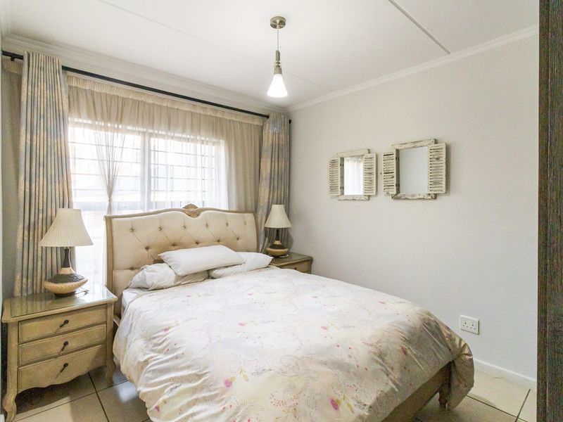 A well-lit bedroom featuring tiled flooring, a window with security bars, and a central ceiling light fixture.
