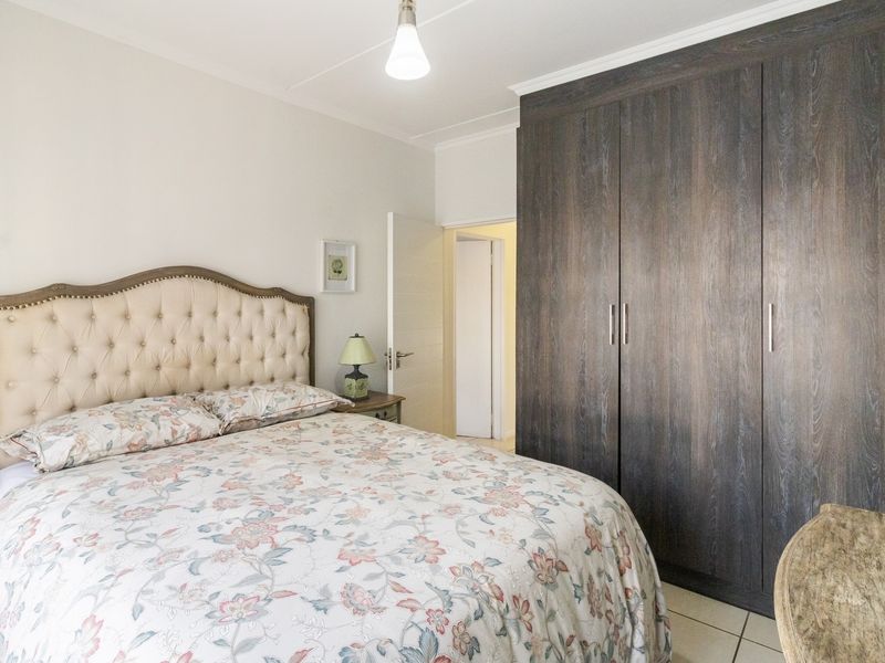 A well-maintained bedroom featuring dark wood-finish built-in cupboards, neutral tiled flooring, and a coved ceiling.