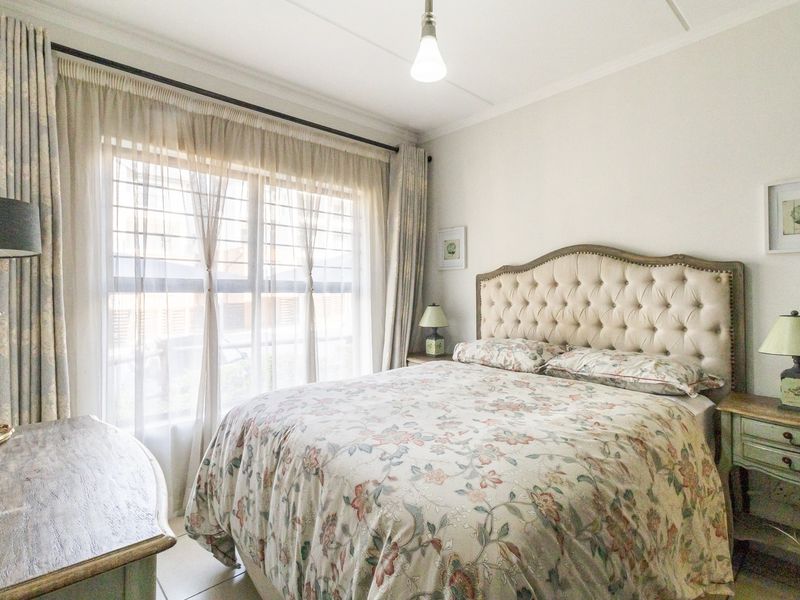 A well-maintained bedroom featuring tiled flooring, large windows with security bars, and neutral wall finishes, providing a comfortable and functional living space.