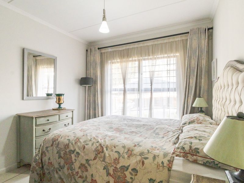 A well-lit bedroom featuring a large window with security gate, neutral walls, and functional electrical fixtures.