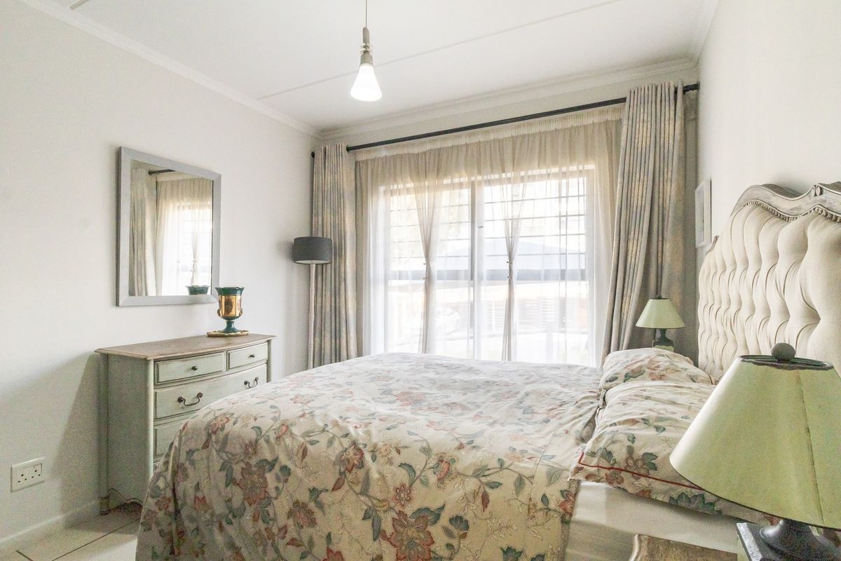 A well-lit bedroom featuring a large window with security gate, neutral walls, and functional electrical fixtures.