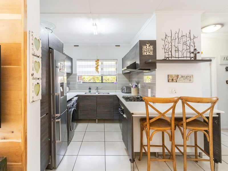 A functional kitchen featuring dark wood-look cabinetry, a gas hob with extractor, tiled backsplash, and a convenient breakfast counter for casual dining.