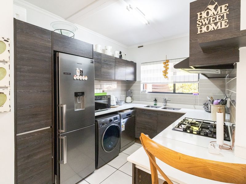 A functional kitchen featuring dark wood cabinetry, a gas hob with extractor fan, double sink, and tiled flooring.