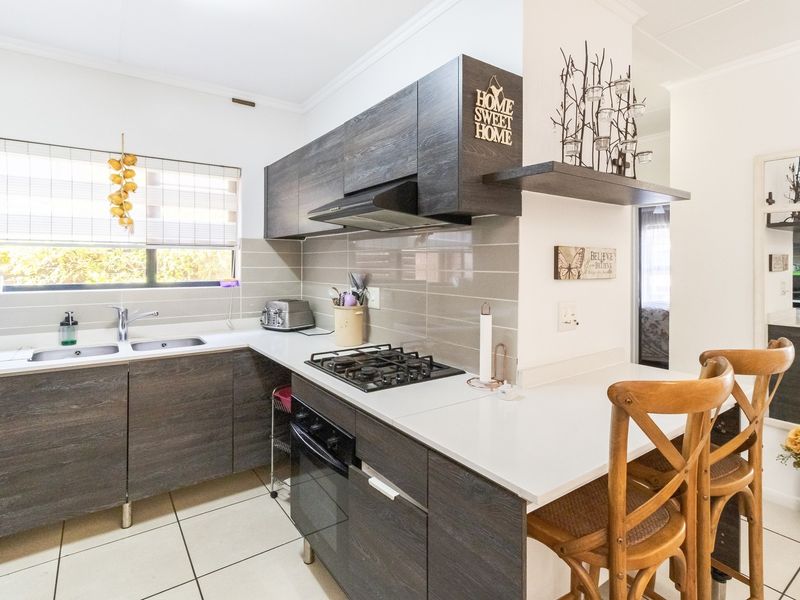 Modern kitchen featuring dark wood-grain cabinetry, stone countertops, gas hob, under-counter oven, and a convenient breakfast bar area.
