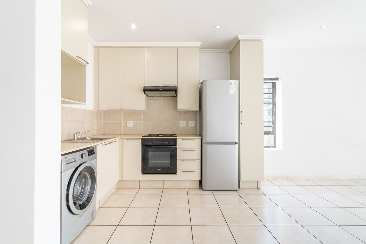 A clean, functional kitchen featuring neutral cabinetry, tiled flooring, built-in oven and hob, and integrated space for laundry appliances.