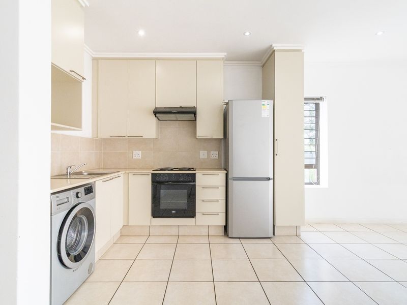 A clean, functional kitchen featuring neutral cabinetry, tiled flooring, built-in oven and hob, and integrated space for laundry appliances.