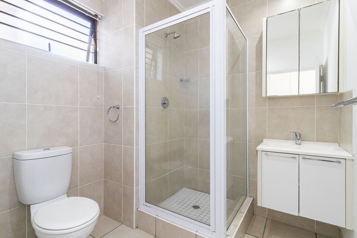 A clean and functional bathroom featuring a glass-enclosed shower, a white vanity with basin, and neutral wall and floor tiling.