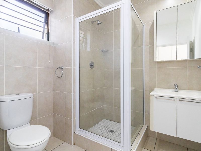 A clean and functional bathroom featuring a glass-enclosed shower, a white vanity with basin, and neutral wall and floor tiling.