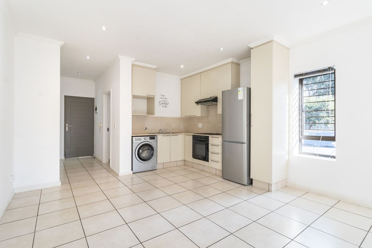 Open-plan kitchen area featuring neutral built-in cabinetry, tiled flooring, and integrated appliances, providing a clean and functional space.