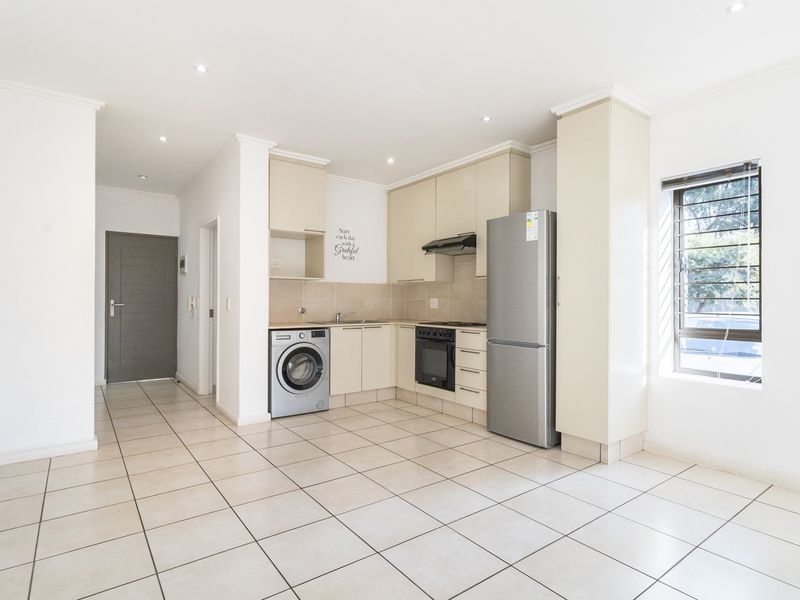 Open-plan kitchen area featuring neutral built-in cabinetry, tiled flooring, and integrated appliances, providing a clean and functional space.