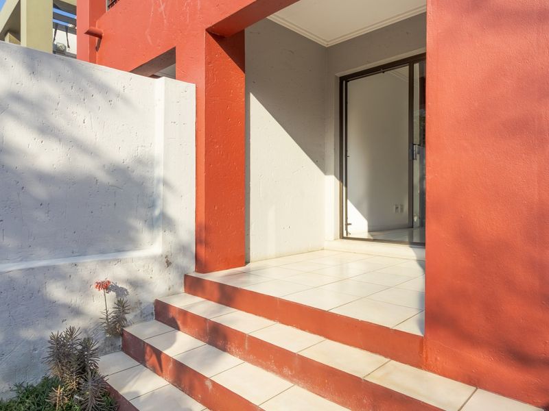 Front entrance featuring tiled steps leading to a sliding glass door, framed by a painted exterior facade and a concrete boundary wall.