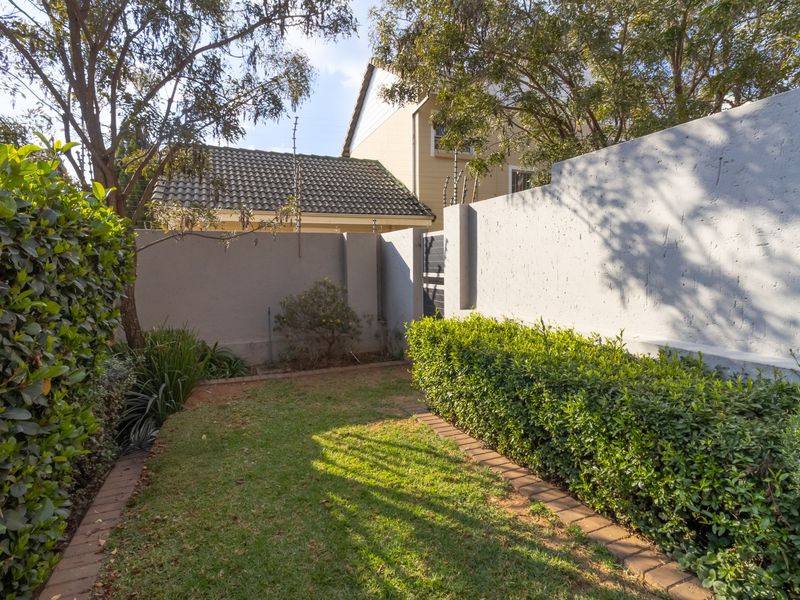 A private garden area featuring a well-maintained lawn, established hedges, and secure perimeter walling with integrated electric fencing.