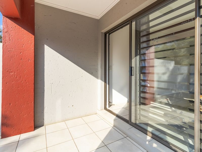 A clean, tiled patio area featuring a sliding glass door with security bars and a prominent red structural pillar.