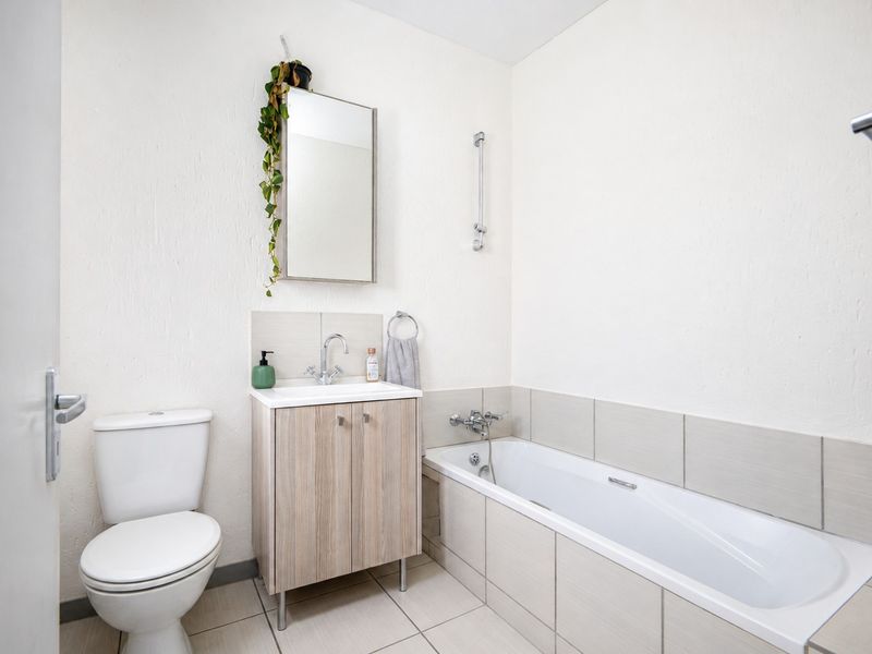 A clean and functional bathroom featuring a built-in vanity, bathtub, toilet, and neutral tiled finishes.