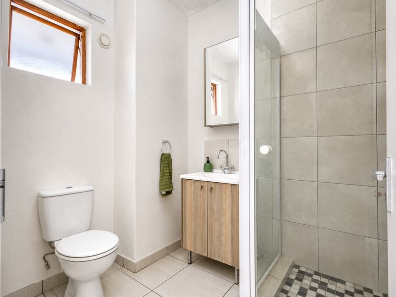 A clean, modern bathroom featuring a glass-enclosed shower, a wood-finish vanity with basin, and neutral wall and floor tiling.