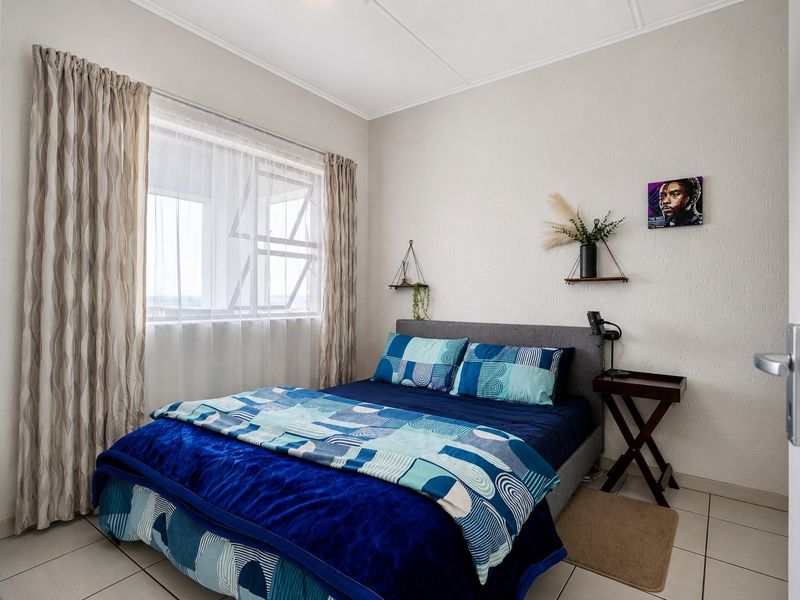 A functional bedroom featuring tiled flooring and a large casement window with installed curtain tracks, providing natural light to the space.