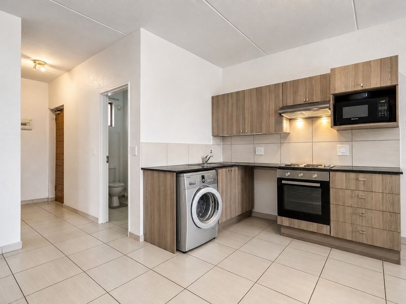 Modern kitchen featuring wood-finish cabinetry, granite countertops, integrated appliances including an oven and hob, and neutral tiled flooring.