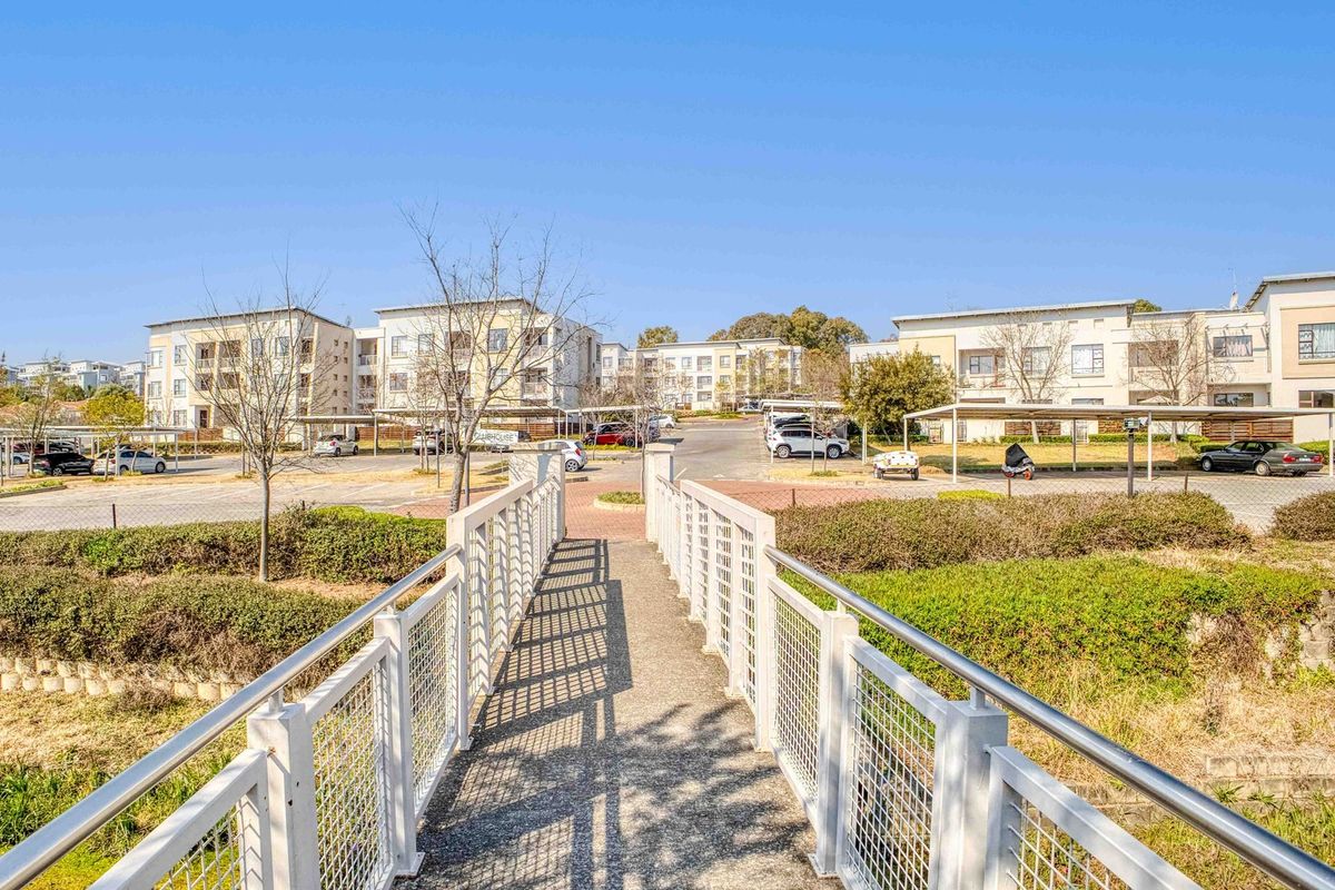 A view of the apartment complex grounds featuring a pedestrian bridge leading towards the parking area and residential buildings.