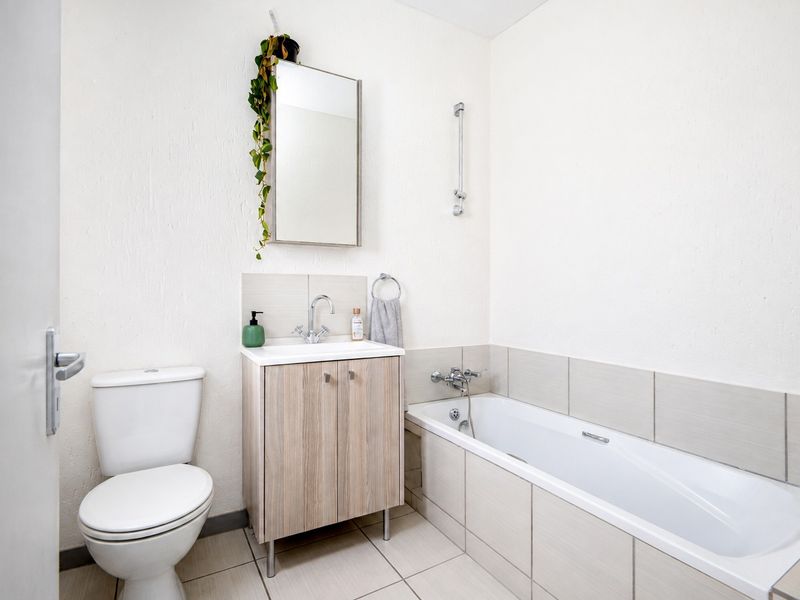 A clean, functional bathroom featuring a white toilet, a wood-finish vanity with a basin, and a tiled bathtub with a shower mixer.