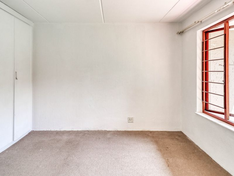 An empty bedroom featuring built-in cupboards, carpeted flooring, and a window with security bars.