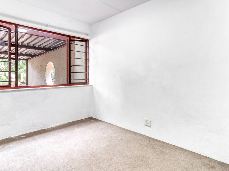 An empty bedroom featuring carpeted flooring, white walls, and a window with integrated security bars looking out onto a covered patio area.