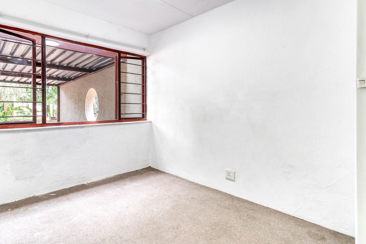 An empty bedroom featuring carpeted flooring, white walls, and a window with integrated security bars looking out onto a covered patio area.