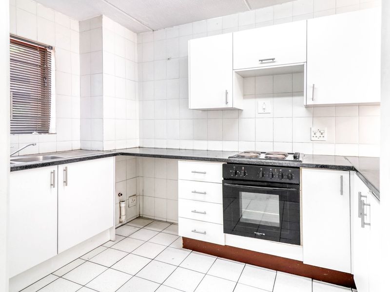 A functional kitchen featuring white cabinetry, granite countertops, a built-in oven with hob, and tiled finishes throughout.