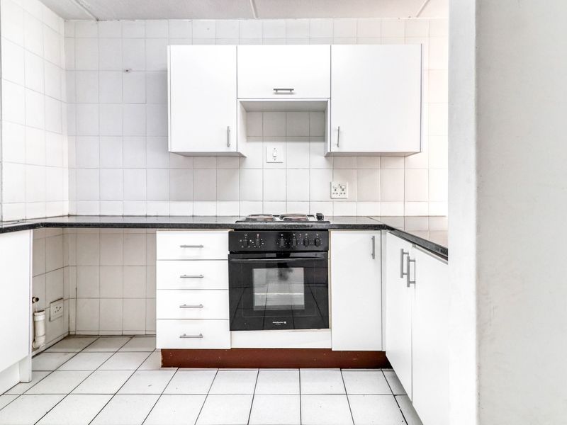 A functional, empty kitchen featuring white cabinetry, black countertops, a built-in oven, and a tiled backsplash, ready for a modern update.