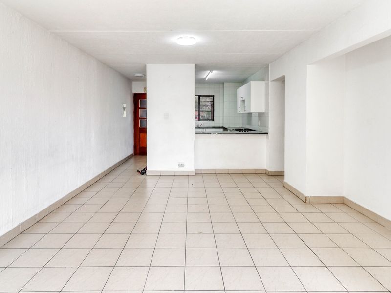 An empty open-plan living and kitchen area featuring tiled flooring, basic built-in cabinetry, and a functional kitchen layout.