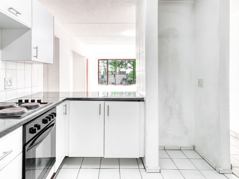 A functional kitchen featuring white cabinetry, a built-in oven with electric hob, stone countertops, and tiled flooring, offering a clean canvas for updates.