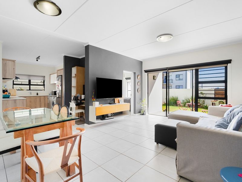 Bright open-plan living and dining area featuring tiled floors, modern kitchen cabinetry, and large sliding glass doors leading to a private outdoor space.