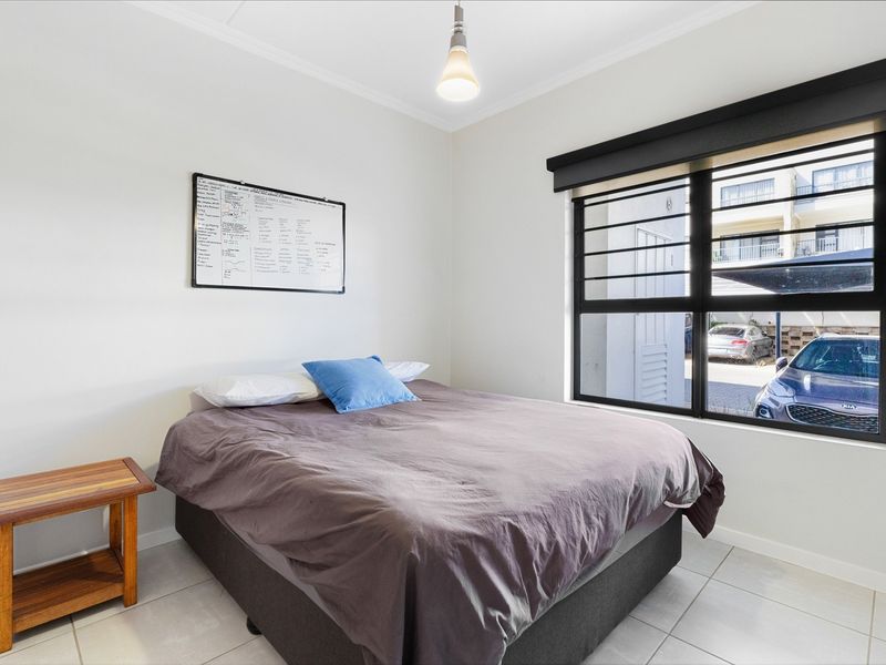 A bright bedroom featuring tiled flooring, a large window with security bars and a roller blind, and a central pendant light fixture.