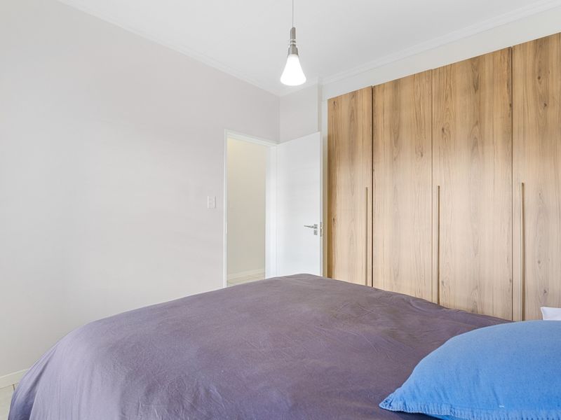 A well-maintained bedroom featuring modern wood-finish built-in cupboards and a clean, neutral aesthetic.