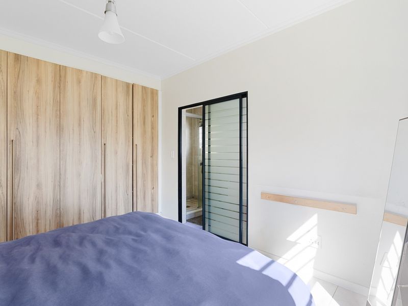 A bright bedroom featuring modern wood-finish built-in cupboards and a sliding door providing access to an en-suite bathroom.