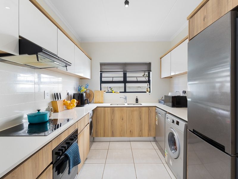 Modern galley-style kitchen featuring sleek white and wood-grain cabinetry, quartz countertops, integrated appliances, and a tiled backsplash with ample storage space.