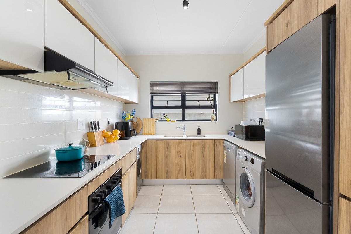 Modern galley-style kitchen featuring sleek white and wood-grain cabinetry, quartz countertops, integrated appliances, and a tiled backsplash with ample storage space.