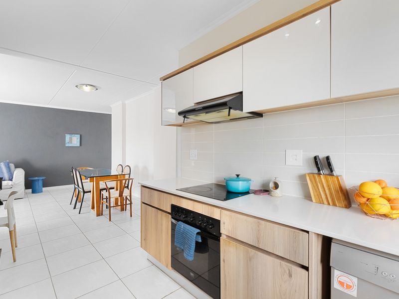 Modern open-plan kitchen featuring sleek cabinetry, integrated appliances, and tiled flooring, seamlessly flowing into the adjacent dining and living area.