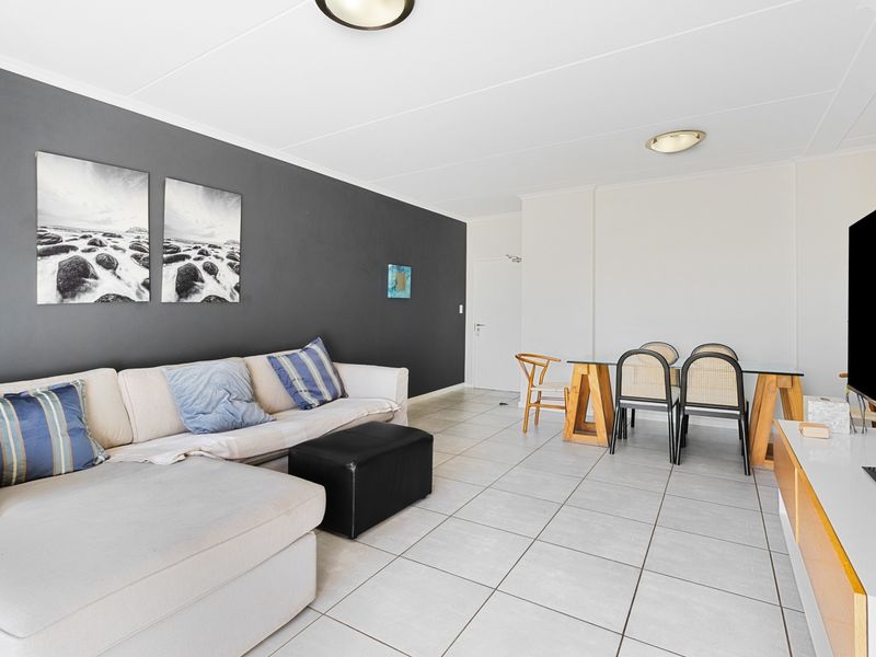 An open-plan living and dining area featuring neutral tiled flooring and a contrasting dark feature wall, providing a versatile space for relaxation and dining.