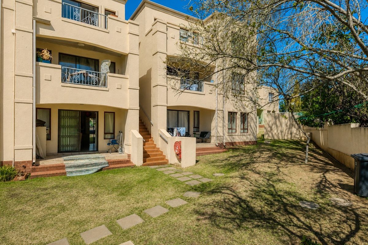 Rear view of the apartment complex featuring ground floor patios, upper-level balconies, and a shared garden area with boundary walling.