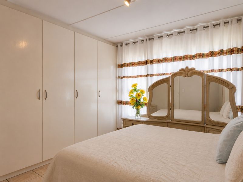 A well-maintained bedroom featuring extensive built-in cupboards and neutral tiled flooring, offering ample storage space and a bright, clean aesthetic.