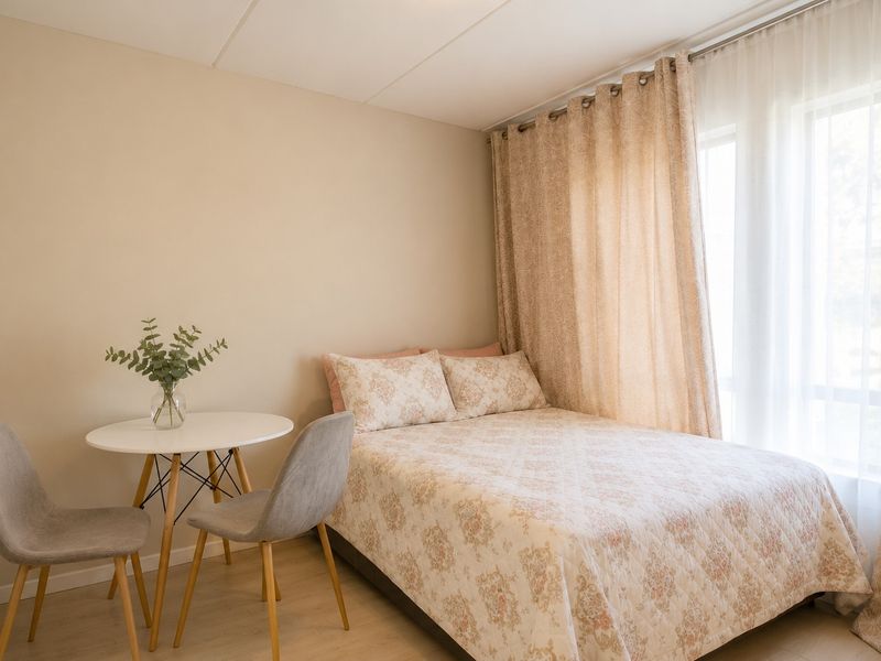 A well-lit bedroom featuring neutral wall tones, laminate flooring, and floor-to-ceiling curtains providing natural light.