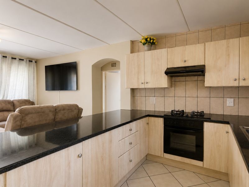 Open-plan kitchen featuring light wood cabinetry, granite countertops, built-in oven, and gas hob, seamlessly flowing into the adjacent living area.