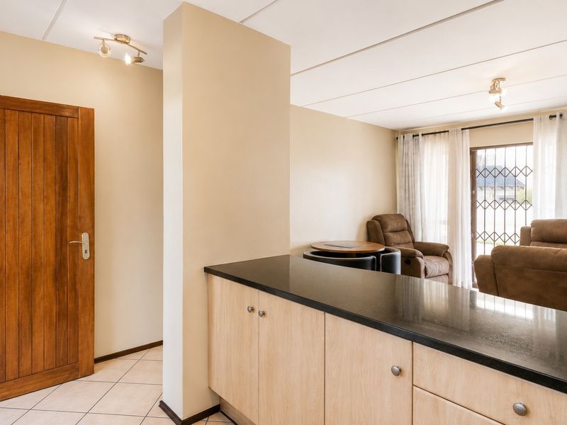 Open plan living area featuring light wood cabinetry with stone countertops, tiled flooring, and access to a patio through a secure sliding door.