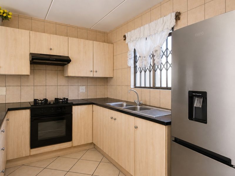 A functional kitchen featuring light wood-finish cabinetry, black granite countertops, a built-in oven with gas hob, and a double basin sink.