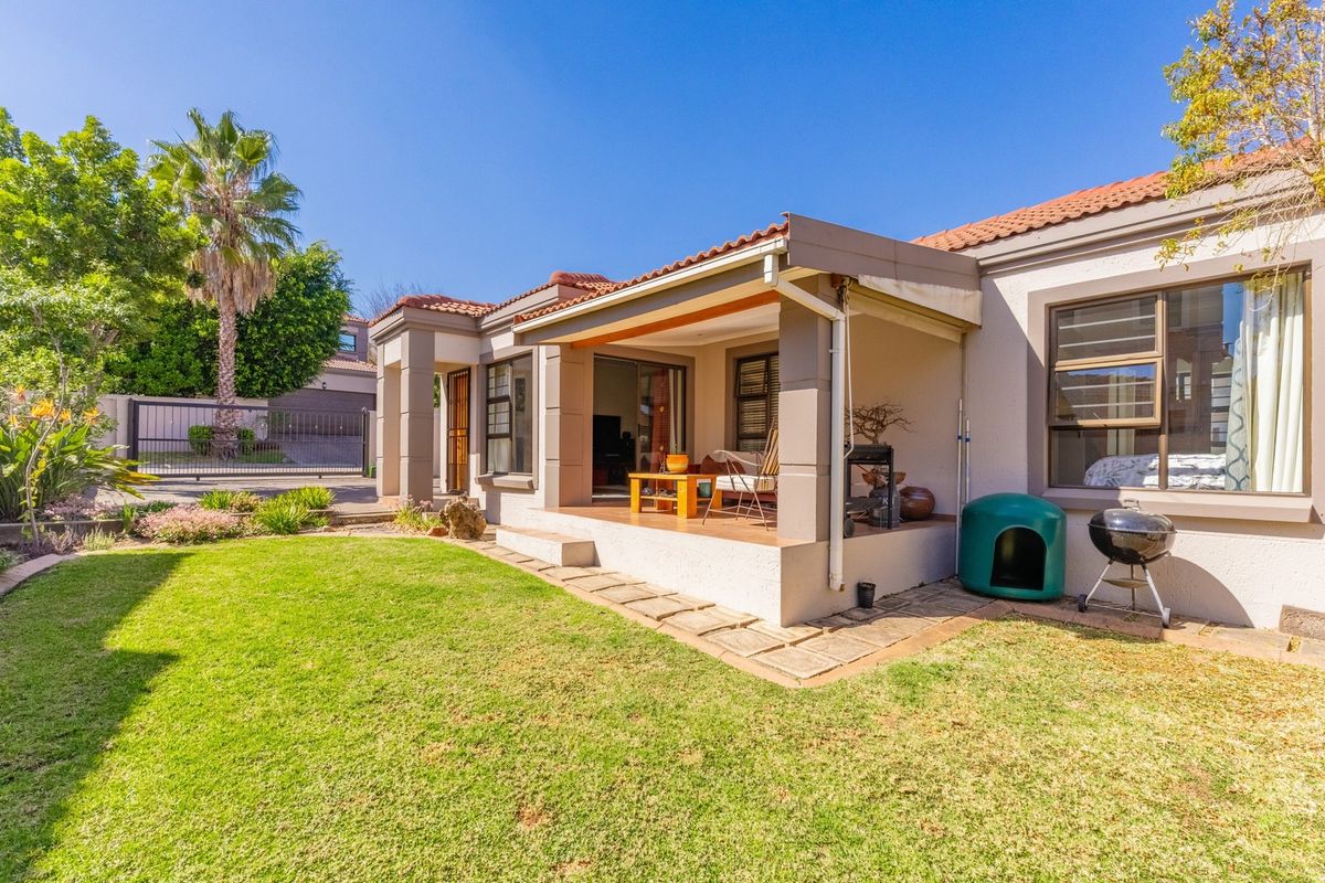 A well-maintained rear exterior view featuring a covered patio, sliding glass doors, and a neat garden area with paved pathways.