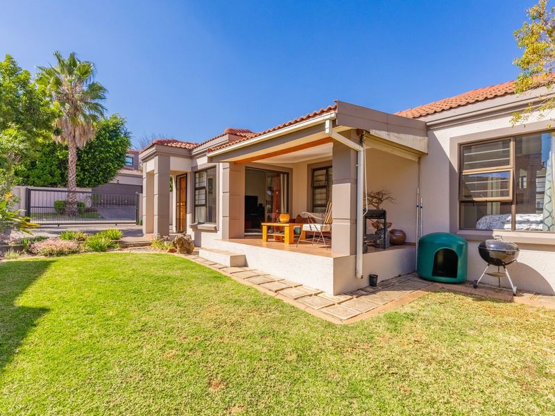 A well-maintained rear exterior view featuring a covered patio, sliding glass doors, and a neat garden area with paved pathways.