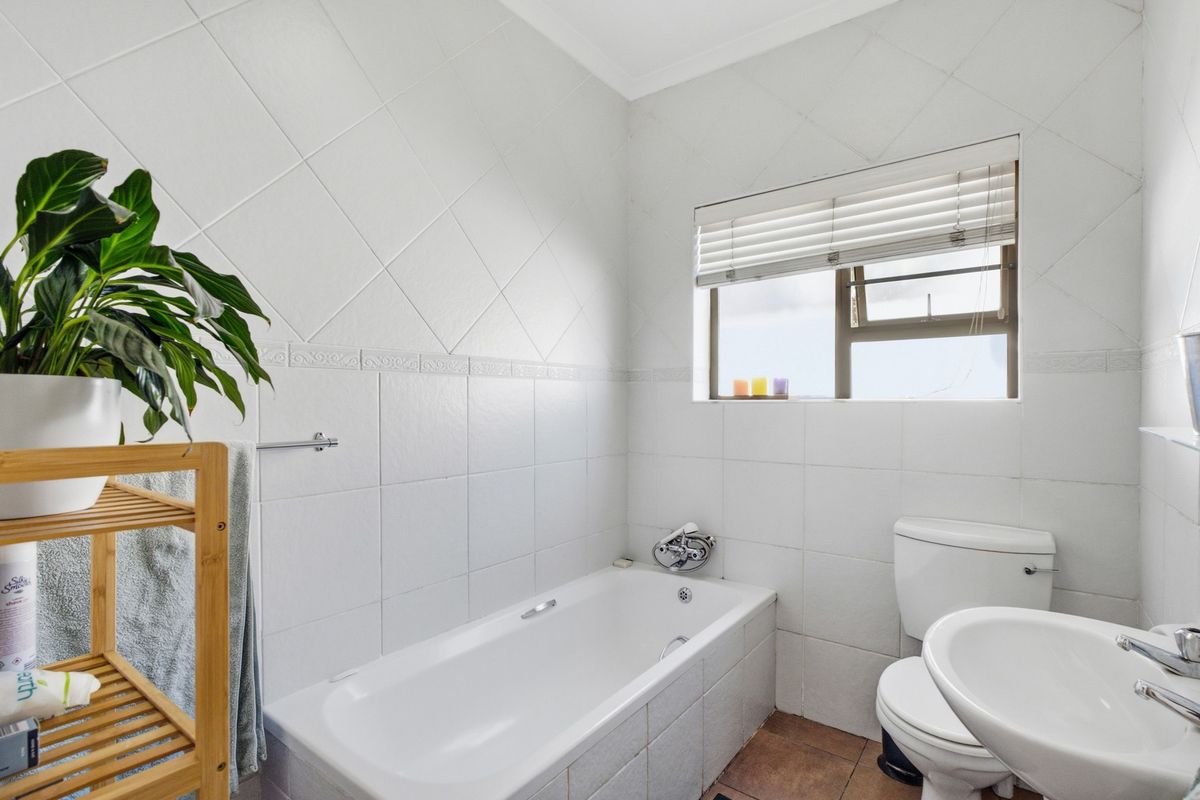 A functional bathroom featuring a bathtub, pedestal basin, and toilet, finished with white wall tiles and contrasting floor tiles.