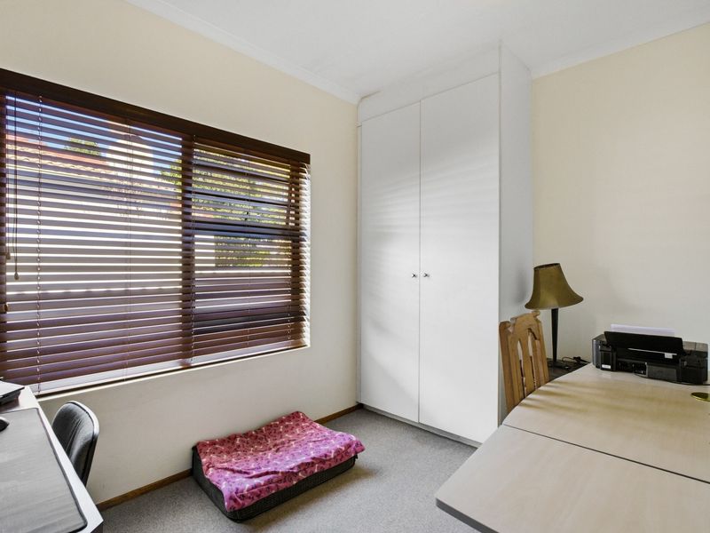 A functional bedroom featuring neutral walls, carpet flooring, a built-in wardrobe, and venetian blinds for adjustable natural light.