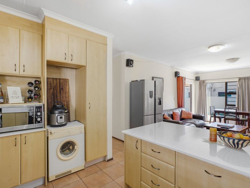 Open-plan kitchen and living area featuring light-wood cabinetry, stone-look countertops, and integrated laundry space, flowing into a comfortable lounge and dining zone.